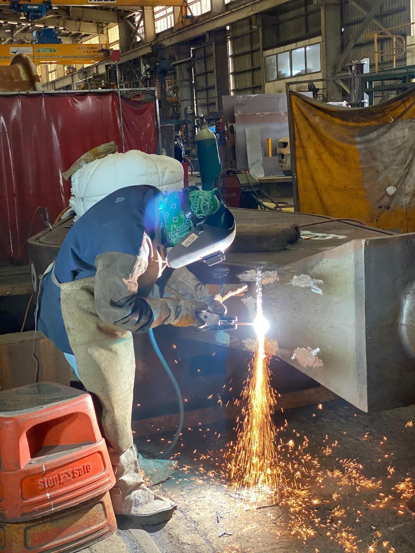 ABC Heavy Engineering boilermaker oxy-cutting a fabricated steel section, sparks streaming, inside the Paget workshop