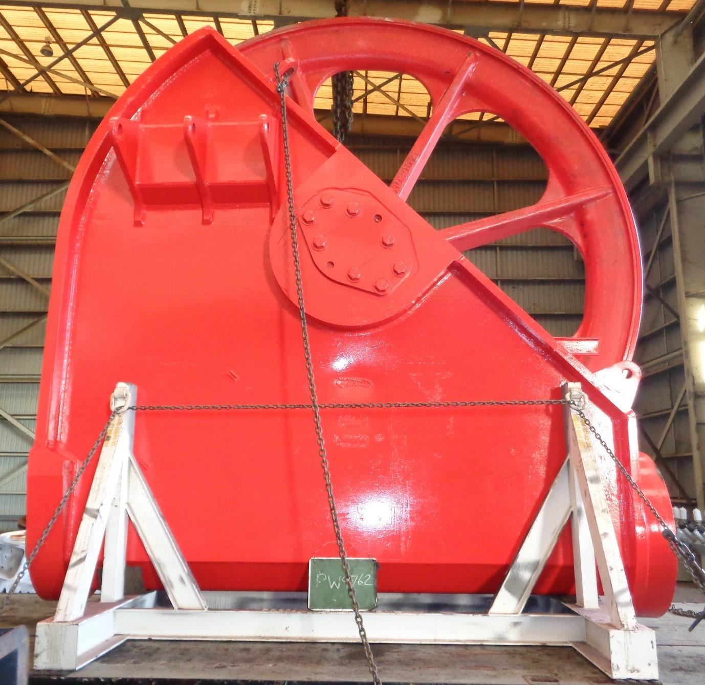 A large dragline sheave wheel finished in fresh red industrial coating, on stands in the paint bay