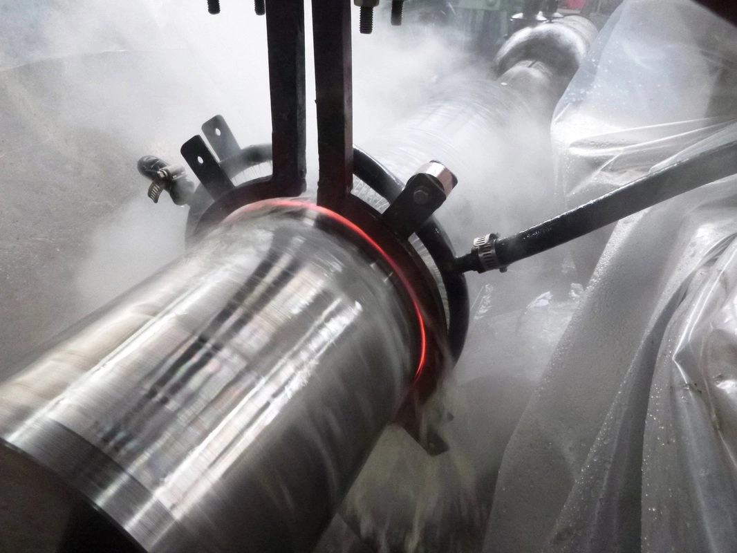 Induction hardening in progress on a rotating steel shaft, a glowing red heat band under the coil