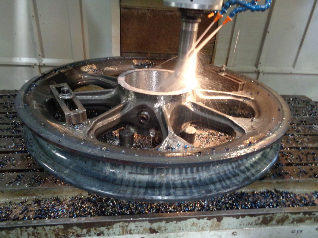 CNC milling machine cutting the hub of a cast wheel component, white-hot sparks at the cutter