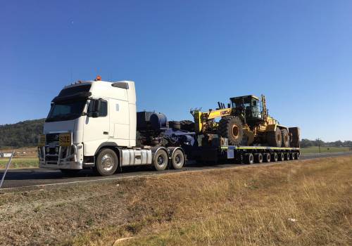 ABC prime mover hauling a Caterpillar grader on a low loader float on a Central Queensland highway