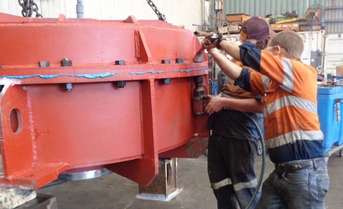 Two ABC Heavy Engineering fitters in hi-vis working together on a large red casing assembly in the Paget workshop
