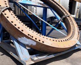 Large-diameter slew bearing ring on support stands in the ABC Heavy Engineering workshop, gear teeth and bolt holes visible